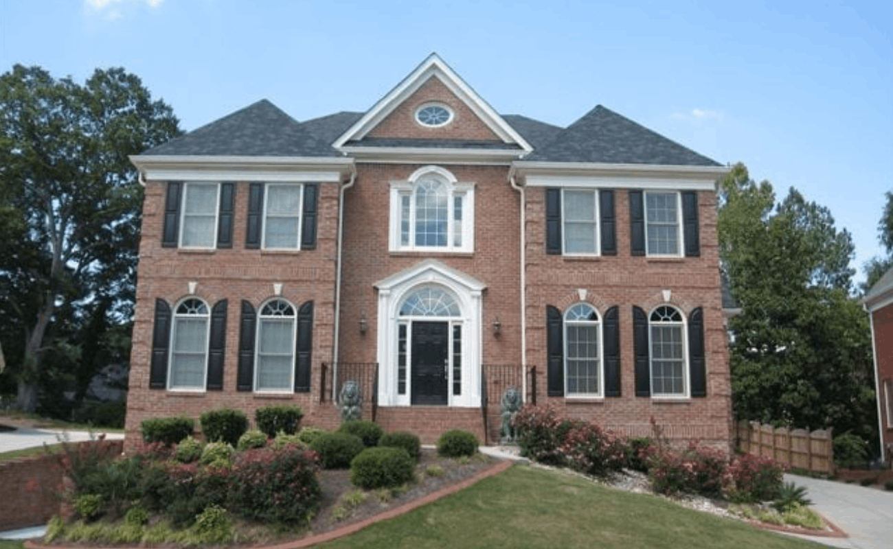 BEFORE installation of front porch with white columns of large brick home with black shutters