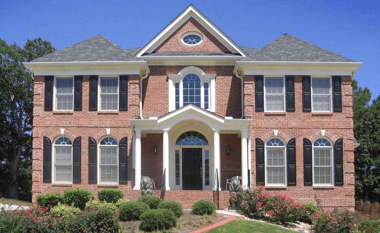 AFTER installation of front porch with white columns of large brick home with black shutters