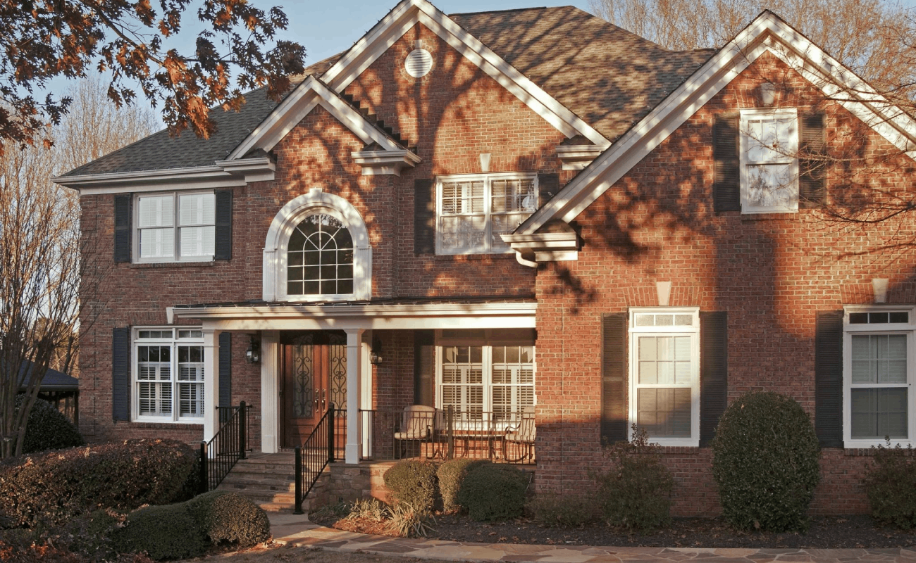 AFTER installation of traditional front porch with white columns of large brick home up close front view