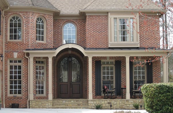 AFTER installation of front porch with tan columns of brick home with brown double doors