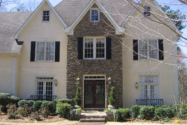 BEFORE installation of traditional half front porch on beige and stone home with brown double doors