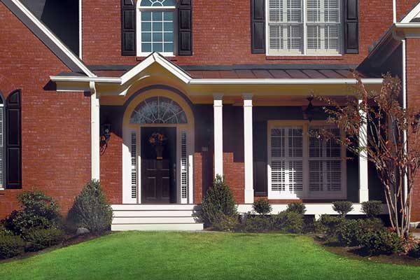 AFTER installation of traditional half porch on large brick home with black shutters up close