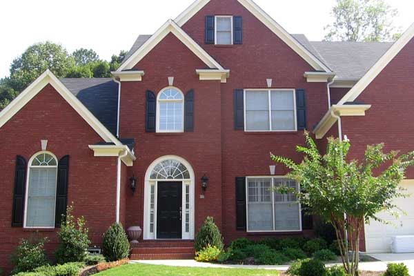 BEFORE installation of traditional half porch on large brick home with black shutters tree on right