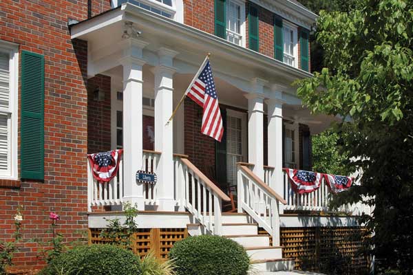 AFTER installation of traditional half porch on large brick home with green shutters up close