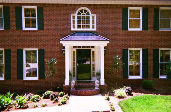 AFTER installation of hip roof portico on brick house with black shutters and glass door