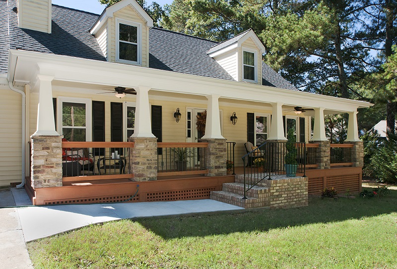 front porch with white columns and stone bottoms light yellow shingled house with black shutters