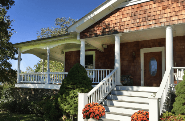 AFTER installation of traditional front porch with white columns on wooden shingled home with white steps