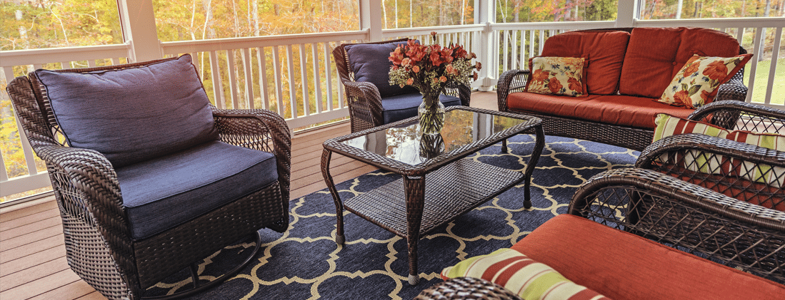 Screened back porch with wicker seating, orange cushions and fall foliage.